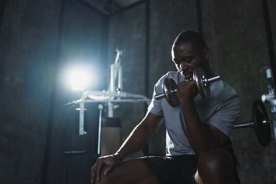 Fitness workout in gym. African American man bodybuilder picking up dumbbells in gym. Workout weight training biceps muscles with dumbbell in fitness club. Man doing sports exercise. Healthy lifestyle - Powered by Adobe