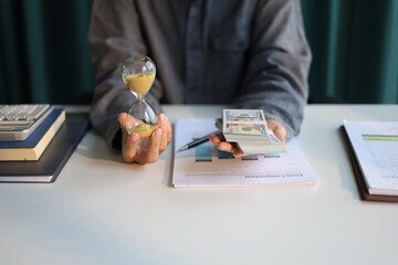 Time and money concept. Businessman holding cash and sand clock imply growth of income, saving or return investment through time.