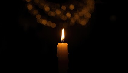 Dark night with a glowing candle flame serving as background decor in religious events and birthday parties, ambient illumination