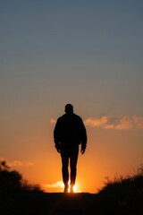 A powerful silhouette of an individual walking across a horizon line against a vibrant, gradient sky, displaying warm orange and yellow hues merging into cooler blues, suggesting either a dramatic sun