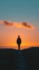 A lone individual's silhouette journeys up a winding path, viewed from behind, against a spectacular sunset or sunrise. The sky is a breathtaking blend of warm oranges and radiant yellows, fading into