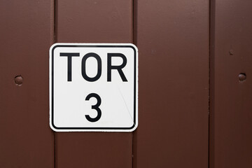 Schild an einer braunen Holzt&uuml;r mit der deutschen Aufschrift Tor 3