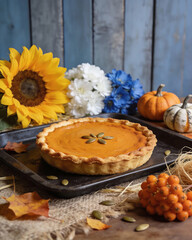 A pumpkin pie sits on a tray next to a vase of flowers and a bowl of berries