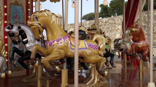 A vintage, richly decorated carousel with golden and black carved wooden horses is set up outdoors, likely in a park or fairground, featuring detailed red and cream accents and illuminated by warm lig
