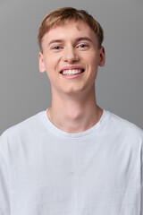 Smiling young man in a white t shirt, casual studio shot with a clean gray background, approachable mood, friendly expression, fresh everyday style, positive vibe and vitality