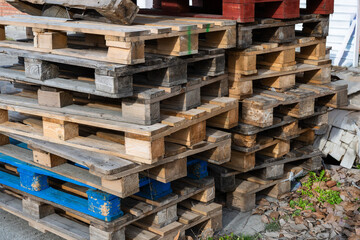 a disorganized stack of used wooden shipping pallets, including a distinct blue one at the base, resting on a paved surface.