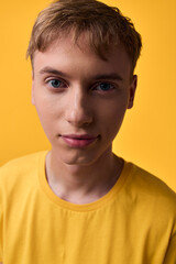 Fototapeta premium Closeup of a young boy wearing a yellow shirt against a warm yellow background, calm expression, soft studio lighting, clear eyes and smooth skin with natural details