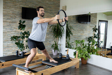 A man demonstrates strength by using a Pilates reformer, emphasizing fitness and balance in a training environment.use an pilates ring on the reformer