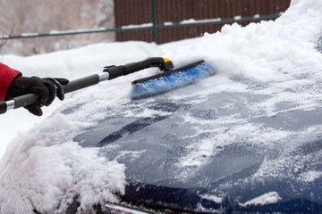 A man brushes snow off his car in winter. Climate, weather.