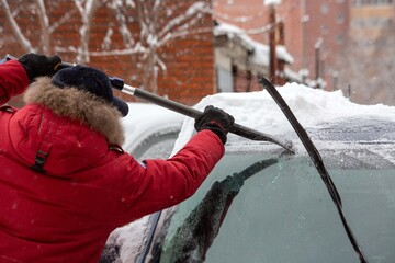 A man scrapes frost off a car window in winter. Climate, weather.