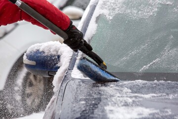 A man brushes snow off his car in winter. Climate, weather.