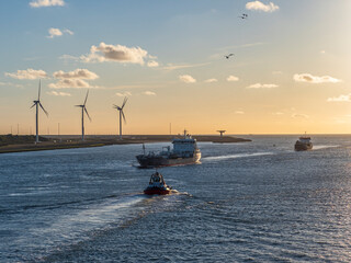 Ships and tugboat sailing at sunset past wind turbines in Rotterdam