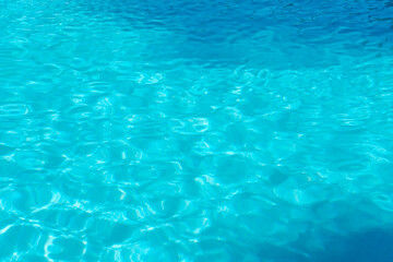 Clear turquoise water ripples in a swimming pool. Sunlight creates a beautiful shimmering pattern. A perfect background for summer vacation.