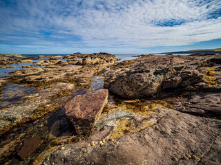 Rocky shoreline with tide pools reflecting cloudy blue sky