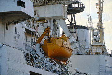 Orange lifeboat mounted on side of an industrial ship, showing maritime safety equipment and rugged naval engineering.