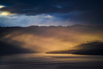 Fototapeta premium Sunbeams breaking through clouds over Scottish loch