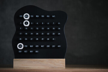 Modern black perpetual calendar on wooden stand with Monday and January 2 highlighted on dark minimalist background.