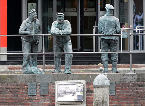 Emden, Germany - July 8 2022 Bronze statues of three retired sailors stand at the harbor railing. They are chewing tobacco. This is a reminder of the 19th-century retirees who also stood 