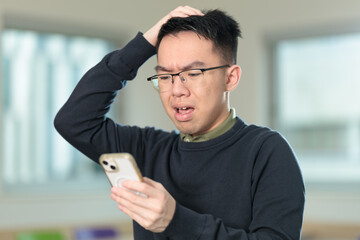 A frustrated Chinese student wearing glasses scratches his head in confusion while looking at his...