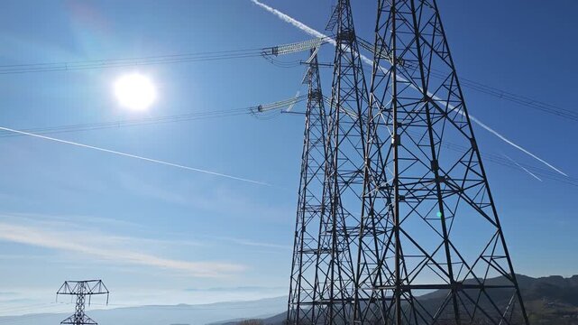 Electricity transmission tower standing tall under a cloudless blue sky on a sunny day. The high voltage power lines extend across the horizon