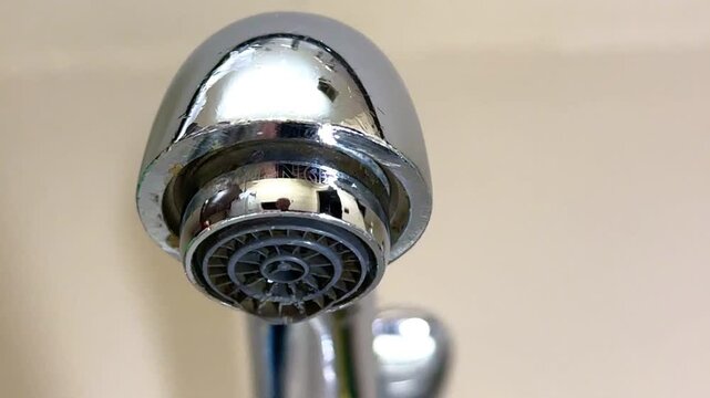 Water Drop From Faucet Aerator.Close-up of a faucet aerator with a falling water drop, symbol of water leak, waste, conservation, saving water, household plumbing problem and sustainability concept.