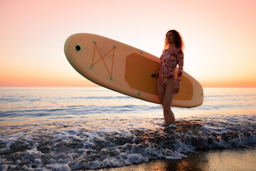 Young woman standing on beach with paddle sup boards during summer vacation