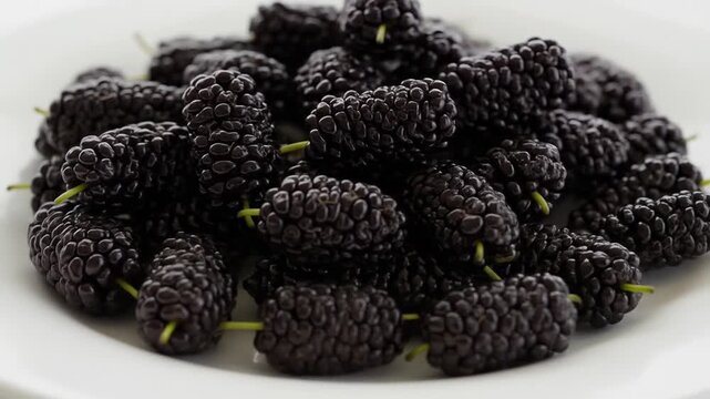 A close-up shot of dark purple mulberries on a white plate