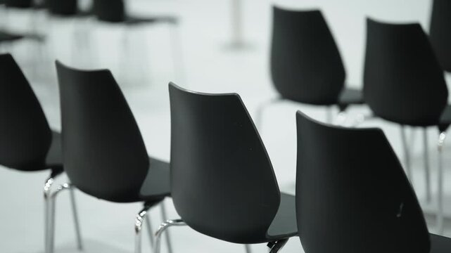 Minimalist black chairs arranged in neat rows within a modern conference space, shown from rear and angled perspectives, highlighting empty seating, repetition, and clean design.