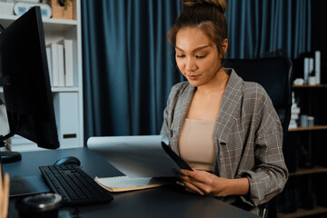 Businesswoman focusing on paperwork folder file on working desk, analyzing market planning database website social media online comparing on computer at over late night at modern office. Infobahn.