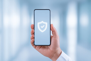 Mobile phone security concept with hand holding smartphone showing shield icon with check mark on screen, digital protection and safe technology in modern office