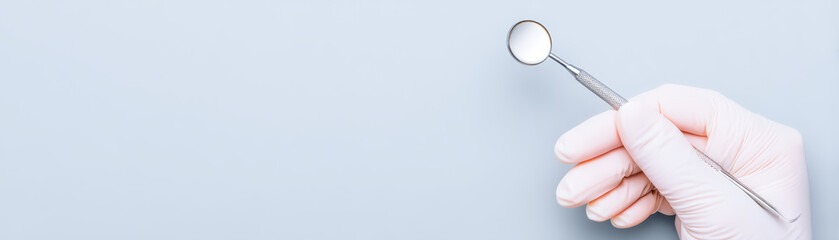 Dental mirror held by gloved hand on light blue background, close up of dental tool for oral examination, minimal style with clean and sterile medical environment
