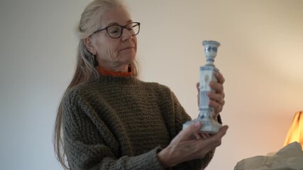 Mature woman unpacks family candlestick heirloom and shares stories of memories tied to each antique in her cozy living space