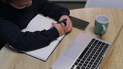 High angle view of a young student diligently writing in a notebook at her desk, with a laptop and smartphone nearby, focusing on the concept of online safety and cybersecurity education - Powered by Adobe