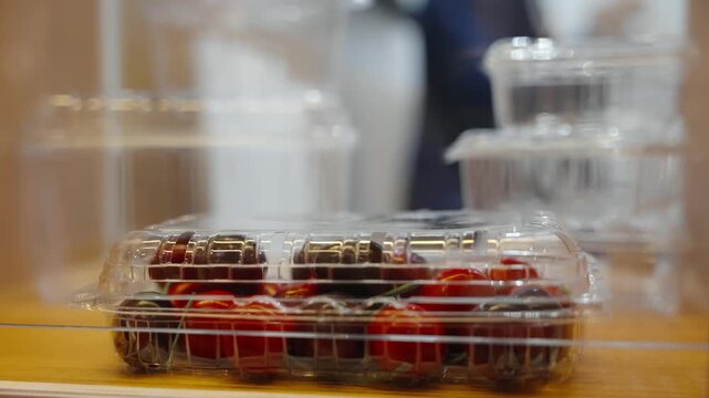 Close-up of plastic clamshell packaged cherry tomatoes on a wooden counter with a blurred background, emphasizing secure storage, product freshness, and a clean, retail display