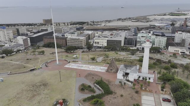 Drone orbits to the left around Donkin Reserve Pyramid and Lighthouse with the coastline in the background on a cloudy afternoon in Gqeberha, Port Elizabeth, South Africa