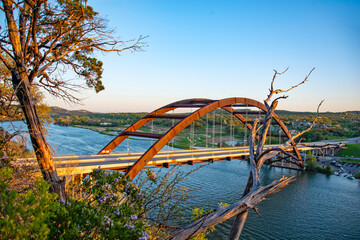 Pennybaker bridge stands over the Colorado river with the sunset reflecting on the water. The blue sky highlights the bridge in the evening light.