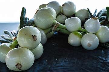 White onions are laid out on a table at a farmers market. Customers browse around looking for fresh produce. The market is lively with vendors and visitors.