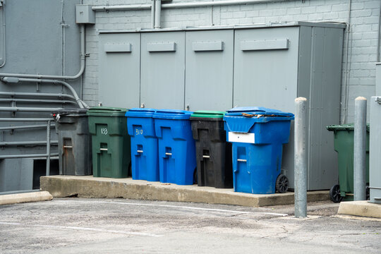 Row of colorful plastic trash cans lined up against a building in an urban alley