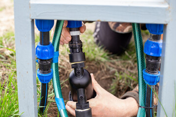 Hands connecting a water filter to a system of pipes and hoses for an automatic drip irrigation system.