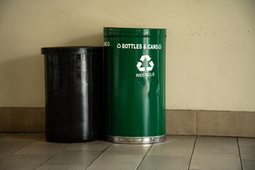 Two recycling bins, one green for bottles and cans, the other black, stand against a wall