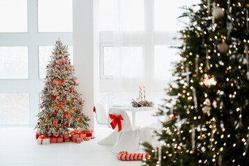 Decorated christmas trees with lights and presents in a bright white room with large windows