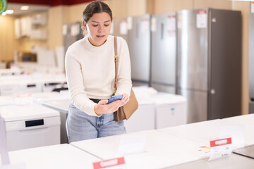 Woman scans a QR code on a washing machine logo to verify information at a supermarket