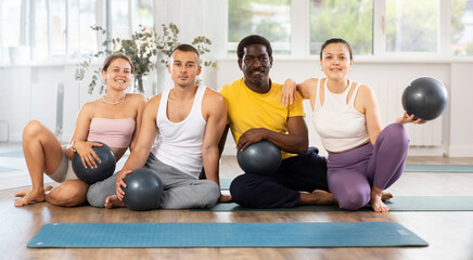 Fototapeta premium Yoga and Pilates teacher poses with multinational students after fit ball session in studio. Report shot, advertising poster for fitness studio
