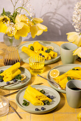 Yellow crepes with blueberries, mint, and lemon slices on pastel plates