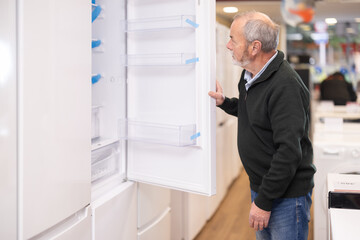 Fototapeta premium Elderly man choose modern fridge at a supermarket
