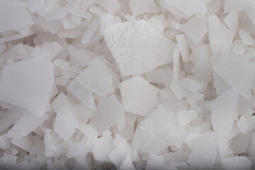White salt flakes magnesium chloride macro background for spa wellness and chemical industry. Close-up of organic mineral crystals used for natural bath treatments and industrial de-icing agent