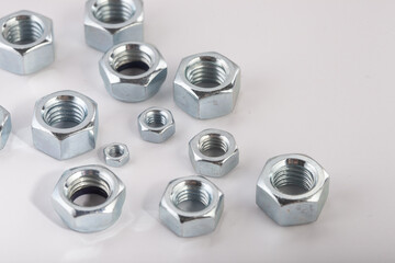 Assorted steel hex nuts on white background for industrial hardware supply and mechanical engineering. Various sizes of metallic fasteners for bolt security construction and technical assembly