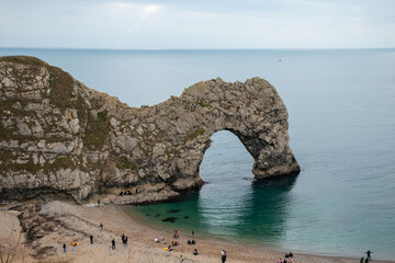 Scenic view of Durdle Door, a striking limestone arch on the Jurassic Coast, attracting tourists for its natural beauty and outdoor activities.