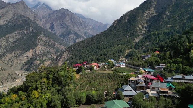 Cinematic aerial shot of a traditional mountain village in the Manali valley, surrounded by cedar forests and snow-capped peaks 