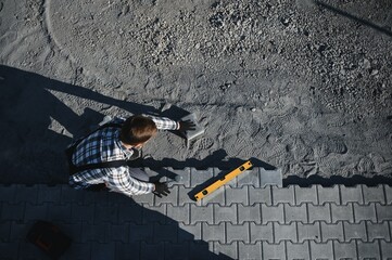 The master in gloves lays paving stones in layers. Garden brick pathway paving by professional...